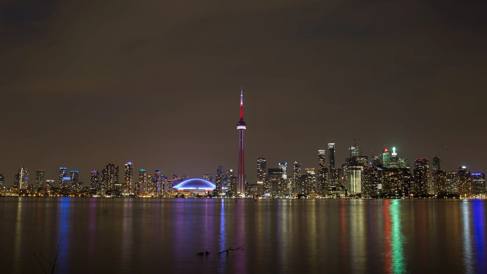 Toronto skyline at night across the water, with downtown towers lit against a dark sky.