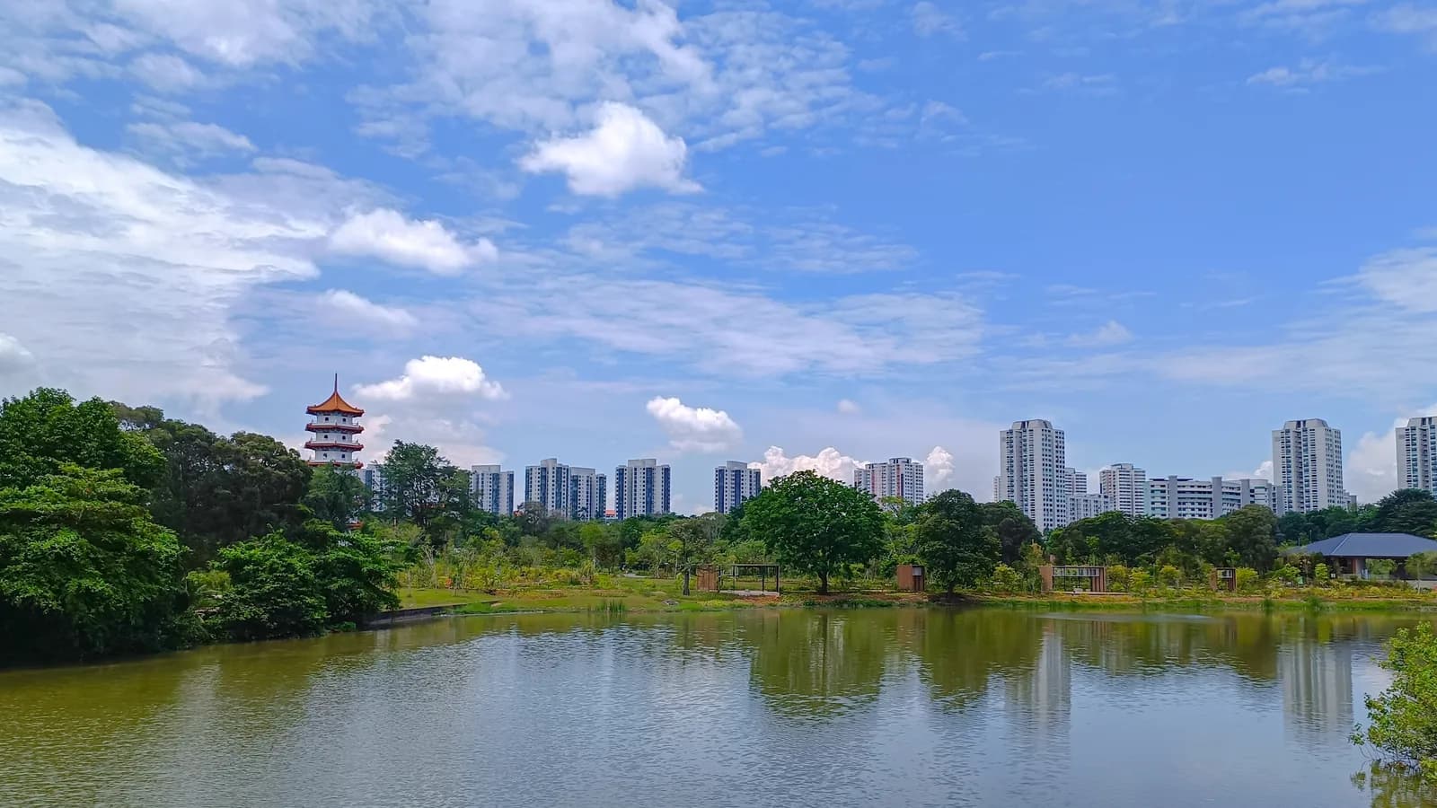 Jurong Lake under a blue sky with scattered cloud, with a red-roofed pagoda on the left and residential towers on the far shore.