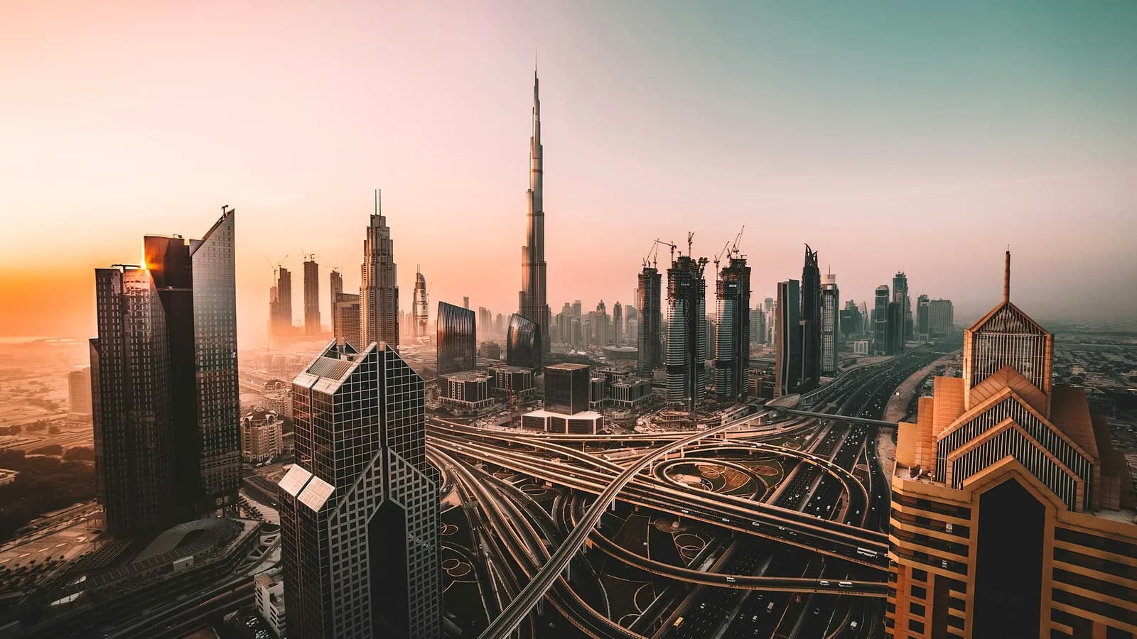 Downtown Dubai from above: highways and towers under a clear sky, with the Burj Khalifa rising in the middle distance.