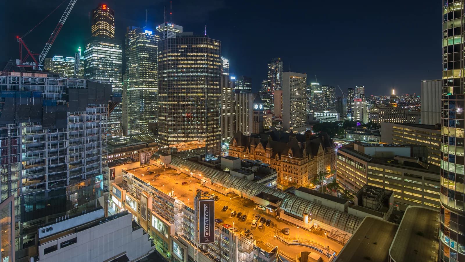 Toronto financial district towers and the old city hall clock tower under a partly cloudy sky, viewed from a high floor.