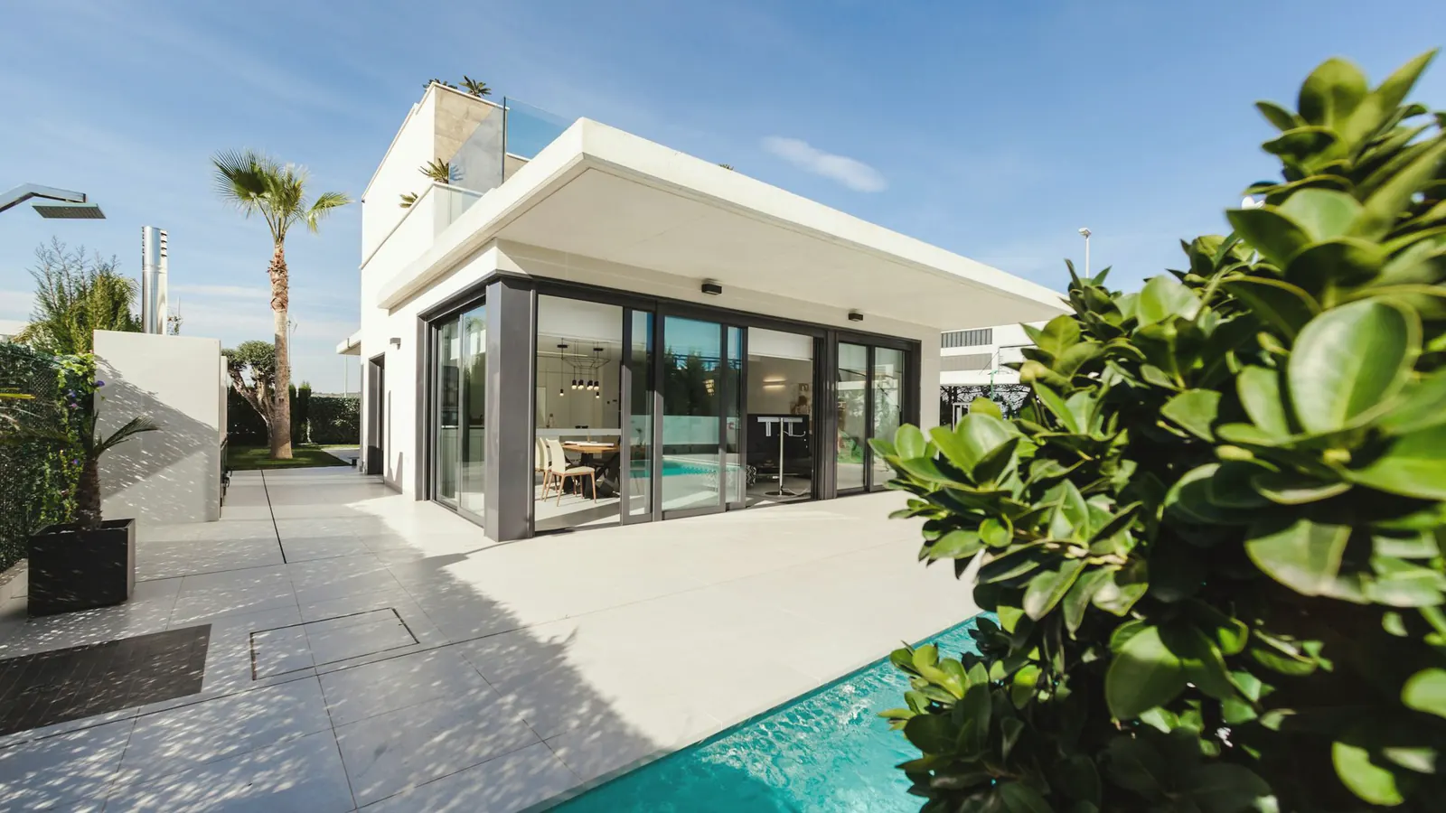 A modern villa at dusk, glass walls lit from inside and a still pool in the foreground.