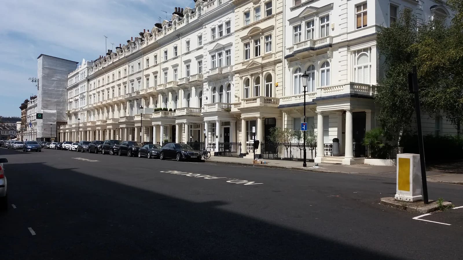 A long terrace of white and cream stucco houses with columned porches and balconies on Queen's Gate Terrace in South Kensington, London, seen from the street on a sunny day