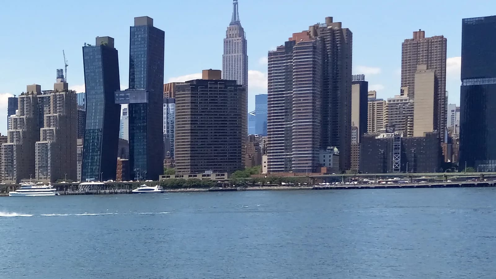 Midtown Manhattan towers, with the Empire State Building at the centre, rising above the East River waterfront on a clear day.