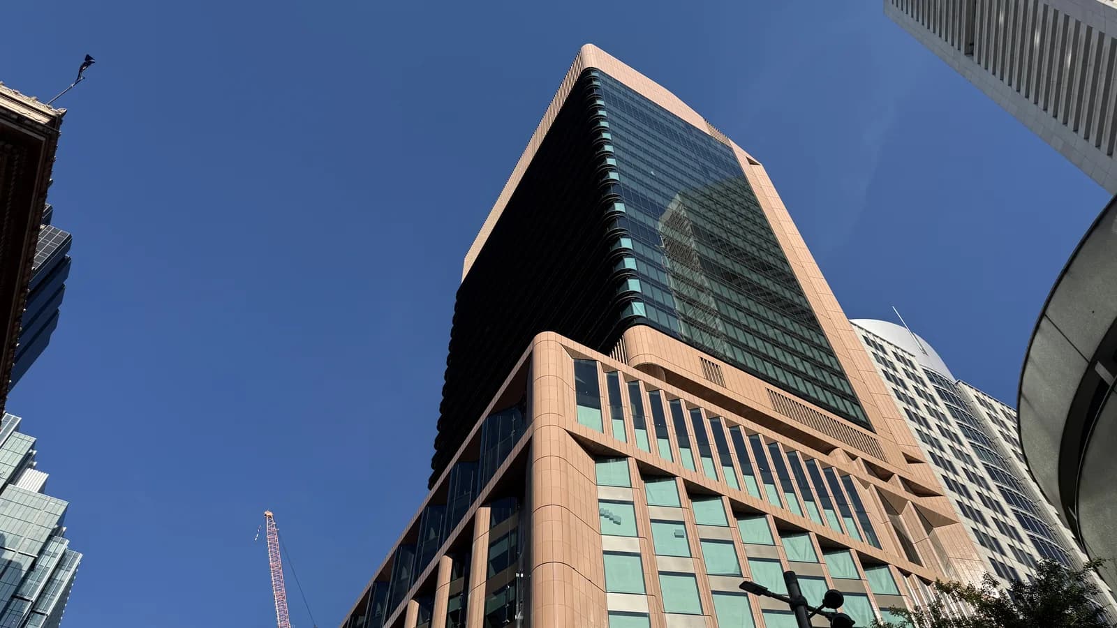 An office tower in central Sydney seen from street level against a clear blue sky, its lower floors clad in pinkish stone with rows of green-tinted windows and its upper floors in dark glass.