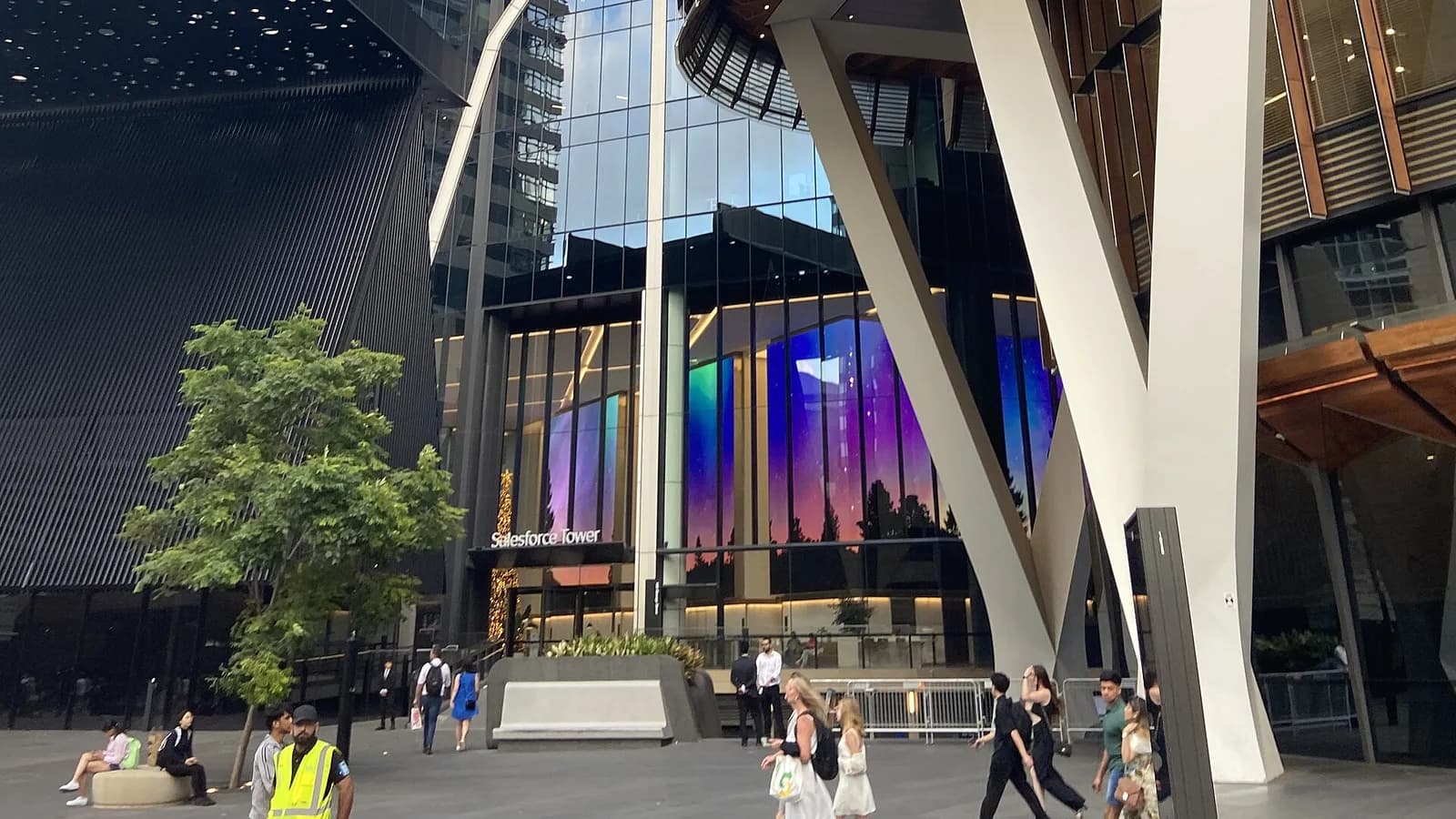 The base of Salesforce Tower in Sydney, with slanted white columns, a curved glass facade and timber-lined soffits above a lobby entrance signed Salesforce Tower, and people crossing the plaza in front.