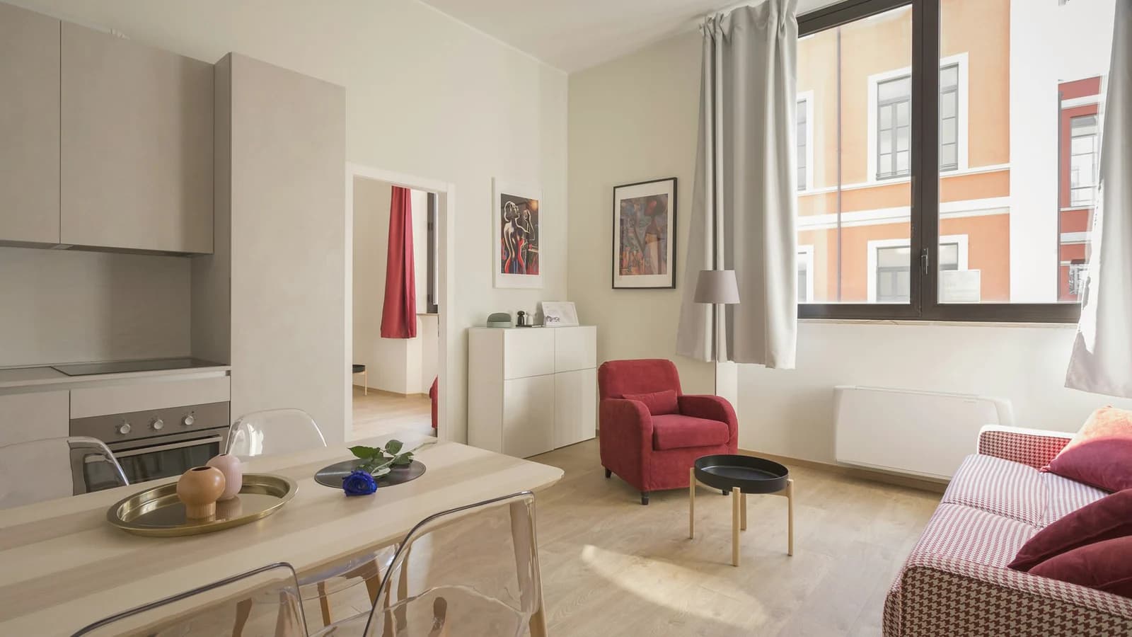 A lived-in apartment in window light, with a red chair, a wooden table, and the city outside.