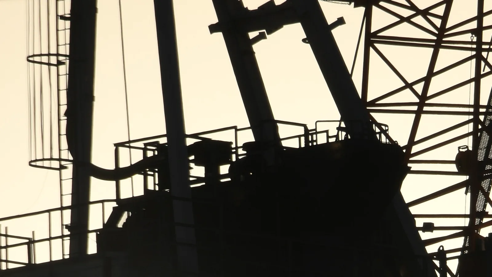 The silhouette of a tower crane's platform and lattice jib against a pale evening sky.