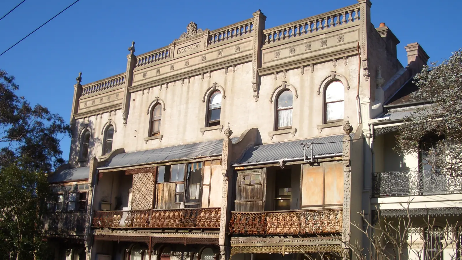 Two-storey Victorian terrace houses with iron-lace balconies and an ornate parapet on a street in Paddington, Sydney.