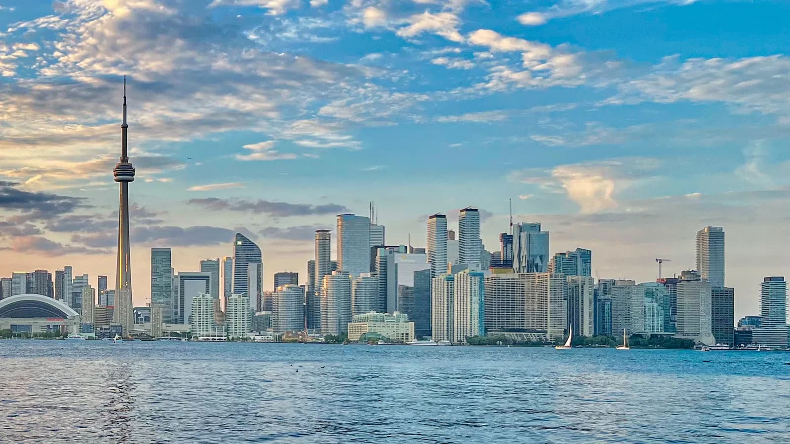 Downtown Toronto towers and the CN Tower seen across Lake Ontario from Centre Island under a partly cloudy sky.